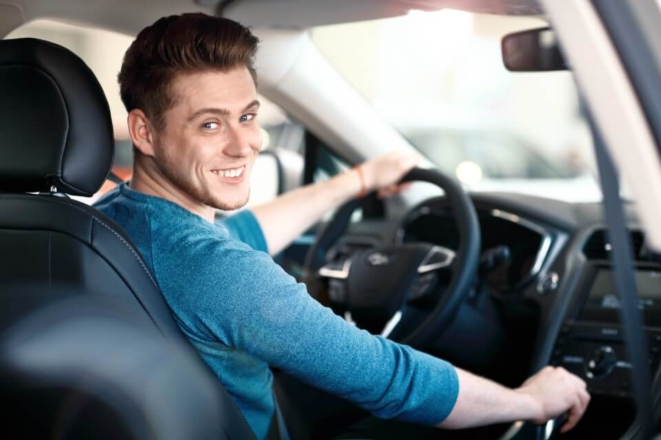 Jeune homme souriant au volant d'une voiture